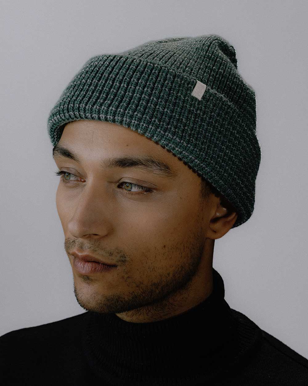 Das männliche Model präsentiert das neue Peak Bagger Beanie in den Farben Grün / Grau