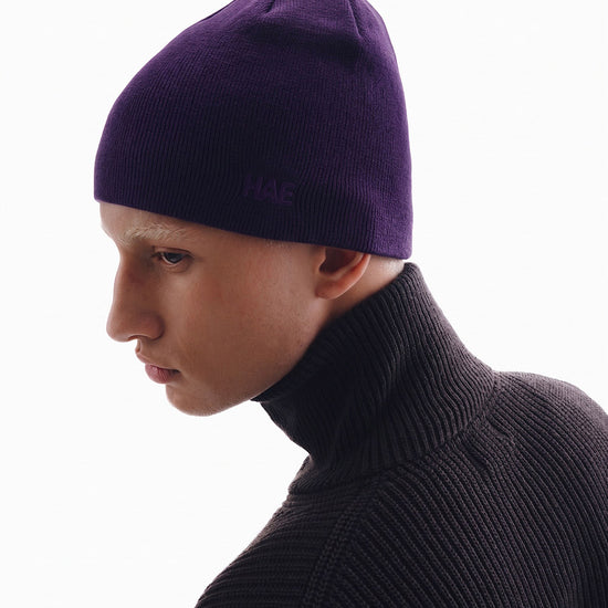 HAE Guide Beanie in Aubergine getragen von einem Model – schlichte Mütze aus weichem Acryl mit Ton-in-Ton gesticktem HAE Logo, Seitenansicht