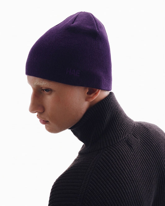 HAE Guide Beanie in Aubergine getragen von einem Model – schlichte Mütze aus weichem Acryl mit Ton-in-Ton gesticktem HAE Logo, Seitenansicht