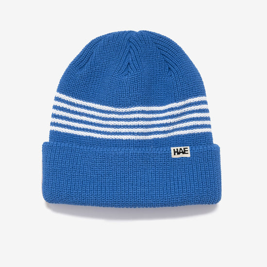 HAE Pathfinder Beanie in Blau mit weissen Ringelstreifen am Bund, HAE-Label, 100% Acryl, freigestellt vor weissem Hintergrund