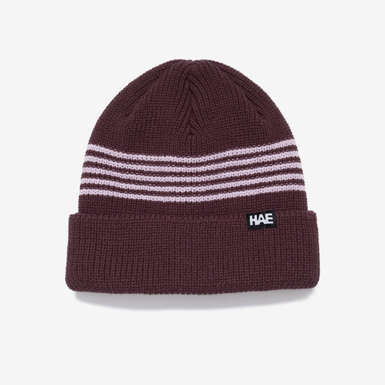 HAE Pathfinder Beanie in Choco mit rosa Ringelstreifen am Bund, HAE-Label, 100% Acryl, freigestellt vor weissem Hintergrund