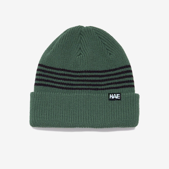 HAE Pathfinder Beanie in Grün mit schwarzen Ringelstreifen am Bund, HAE-Label, 100% Acryl, freigestellt vor weissem Hintergrund