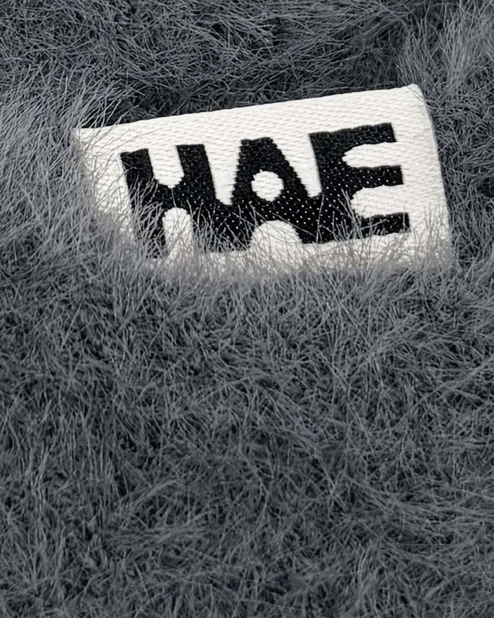 Adventurer 2.0 Mütze von HAE in Dunkelgrau – Detailaufnahme des HAE-Labels auf dem flauschigen Polyamid-Gewebe