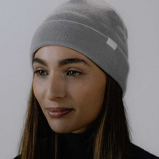 Das weibliche Model präsentiert die graue Variante der Mütze Merino