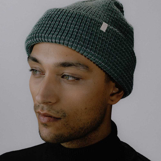 Das männliche Model präsentiert das neue Peak Bagger Beanie in den Farben Grün / Grau