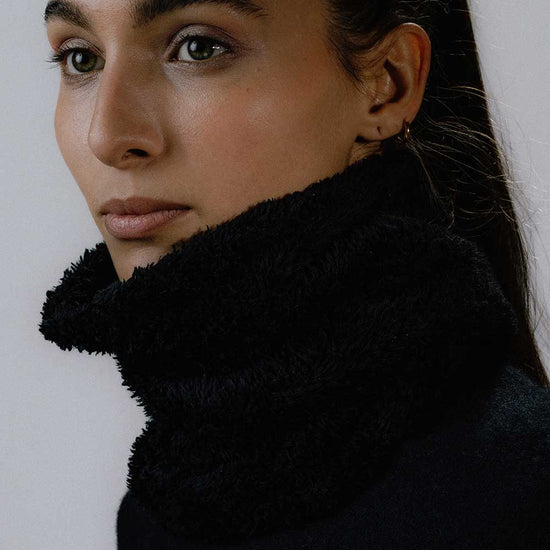 Das weibliche Model trägt den Wellness Neckwarmer in Schwarz
